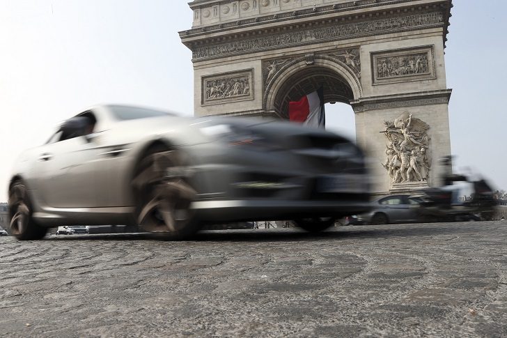 Cars and scooters drive around the Arc de Triomphe, seen in background, in the center Paris, France, Wednesday, March 18, 2015. Paris police have lowered the speed limit and ordered a halt to burning of trash as part of emergency measures triggered by a spike in air pollution, months before the city hosts a major international climate conference. (AP Photo/Francois Mori)
