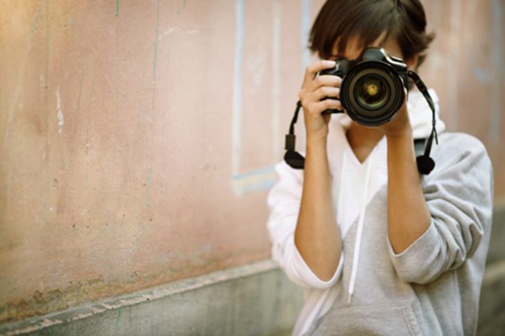 female photographer with professional SLR camera, natural light, selective focus on nearest part of lens with blend